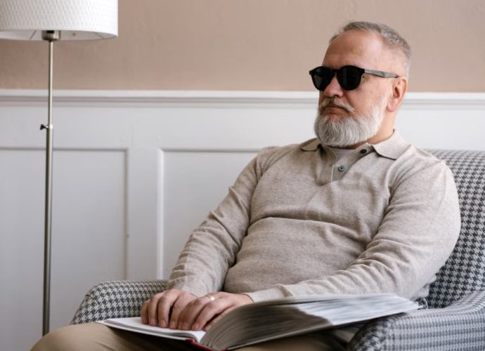 Senior man with sunglasses reading a braille book in a cozy modern interior.