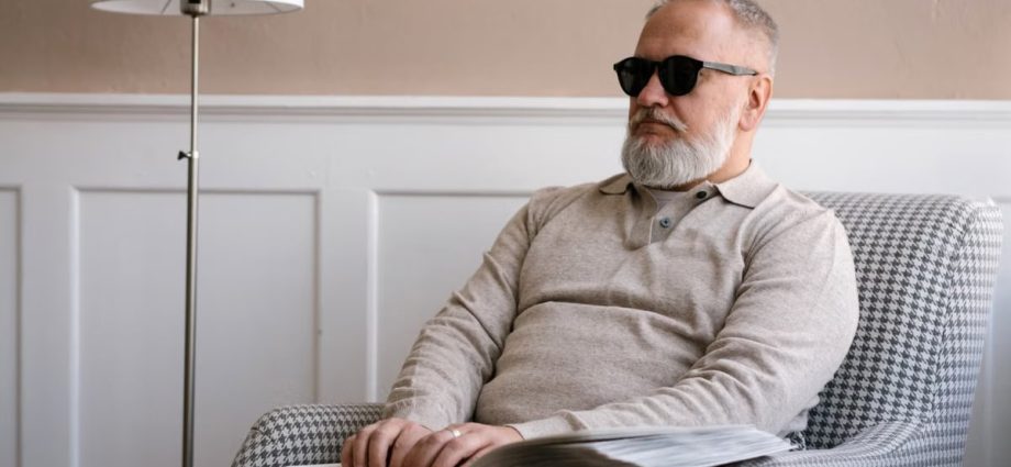 Senior man with sunglasses reading a braille book in a cozy modern interior.