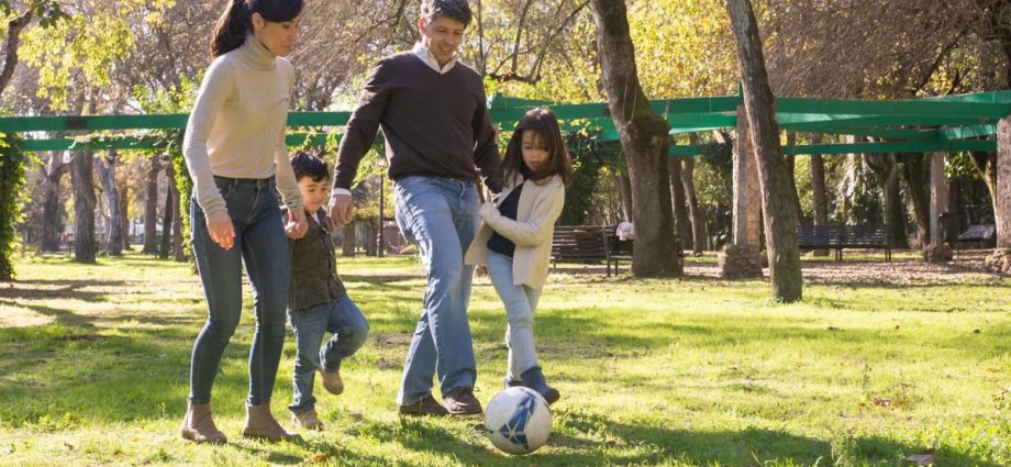 A family plays soccer together in a sunny park, enjoying quality time outdoors.